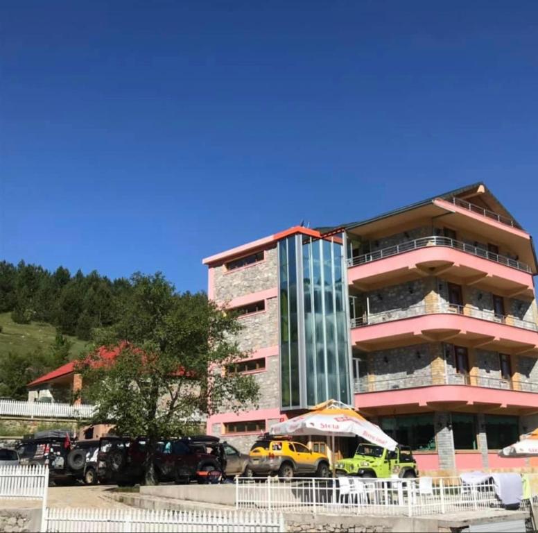 un grand bâtiment avec des voitures garées devant lui dans l'établissement LURA Hotel, à Peshkopi