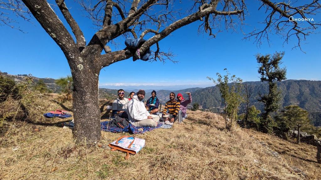 a group of people sitting on a hill under a tree at Shoonya Mukteshwar in Mukteswar