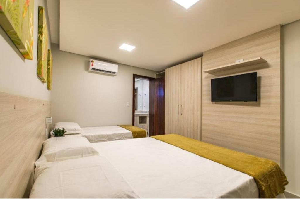 Habitación de hotel con 3 camas y TV de pantalla plana. en Hotel Encantos de Itaperapuã, en Porto Seguro