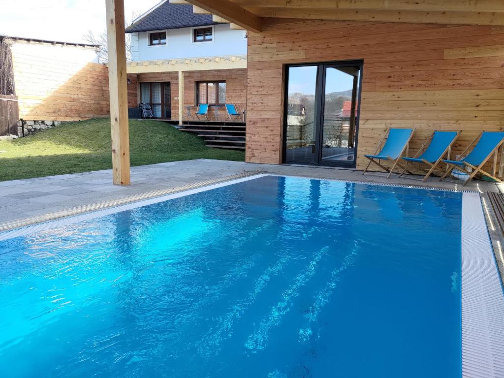 a swimming pool with blue chairs and a house at Švihák lázeňský in Velké Losiny