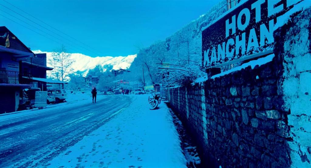 Hotel Kanchani - A Majestic Mountain Retreat في مانالي: شخص يسير في شارع مغطى بالثلج بجوار مبنى