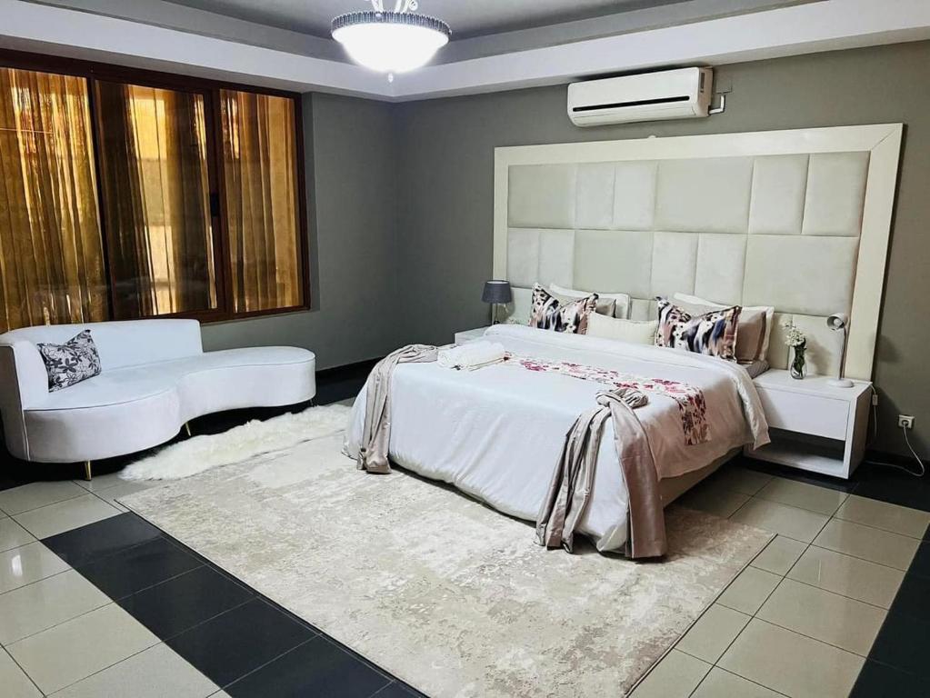 um quarto com uma grande cama branca e um sofá em TR GUEST HOUSE em Matola