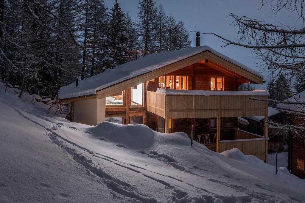 una cabaña de madera en la nieve con las luces encendidas en Chalet Adler, en Saas-Fee