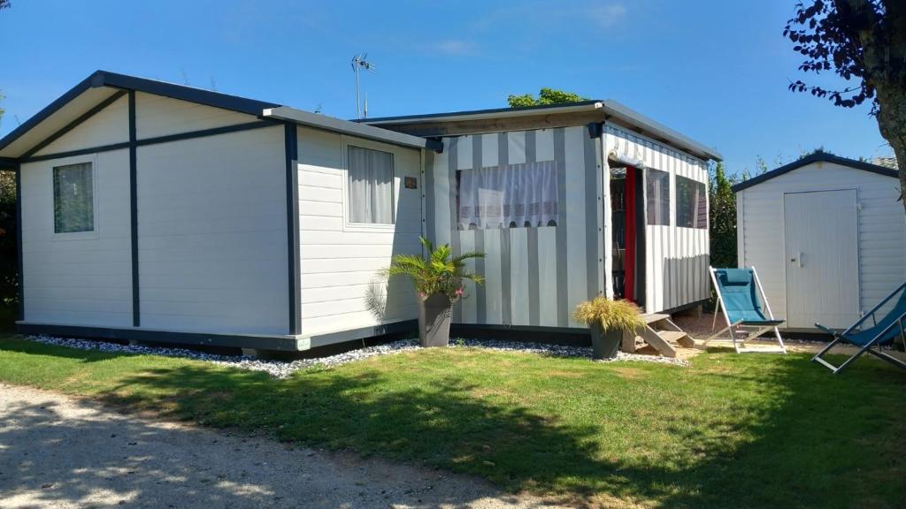 un petit hangar blanc avec une chaise dans la cour dans l'établissement Charmant chalet situé dans un camping 4 étoiles - 4 à 6 personnes - TILIO, à Guidel