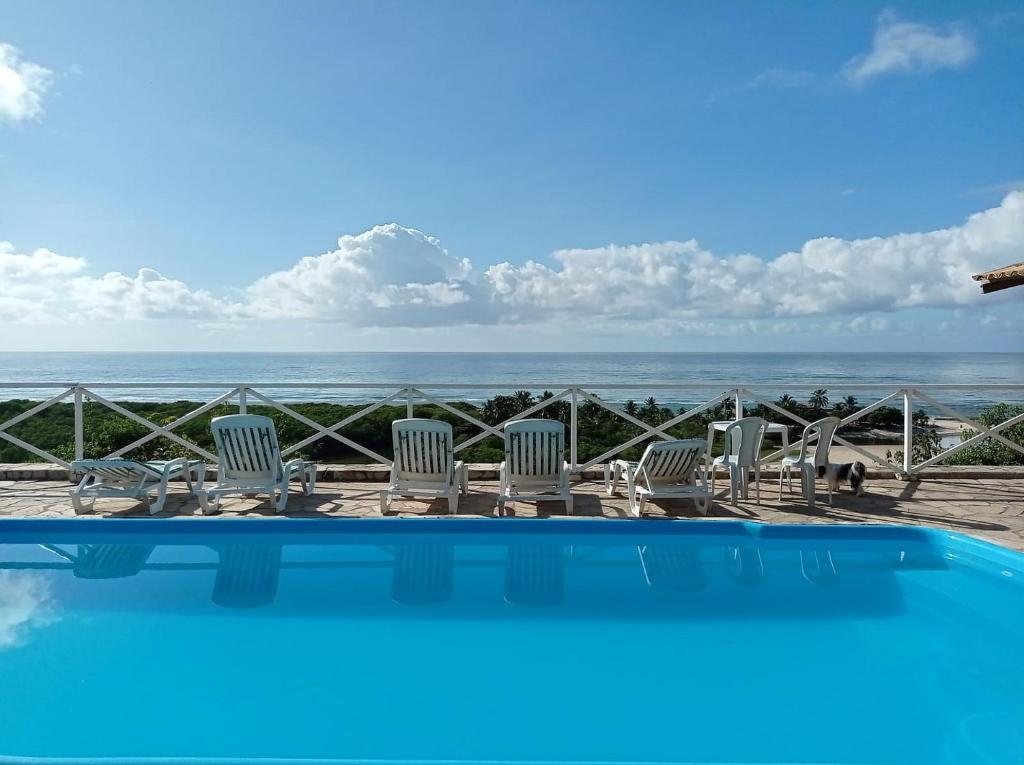 a pool with chairs and a view of the ocean at Pousada Portal dos Coqueirais in Jequia da Praia