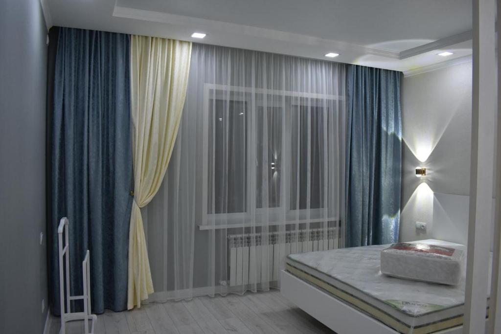 Schlafzimmer mit einem Bett mit blauen Vorhängen und einem Fenster in der Unterkunft VIP квартира in Oral