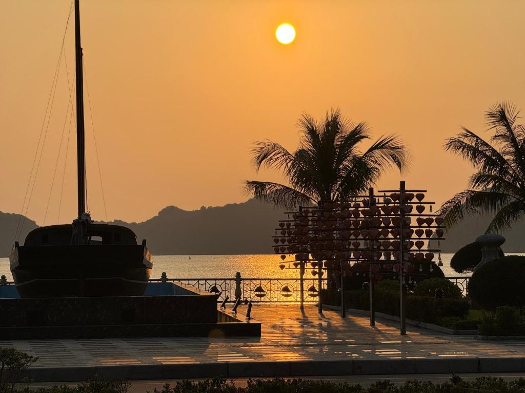 zachód słońca nad wodą z palmami i łodzią w obiekcie Phoenix Flower Hotel w mieście Cát Bà