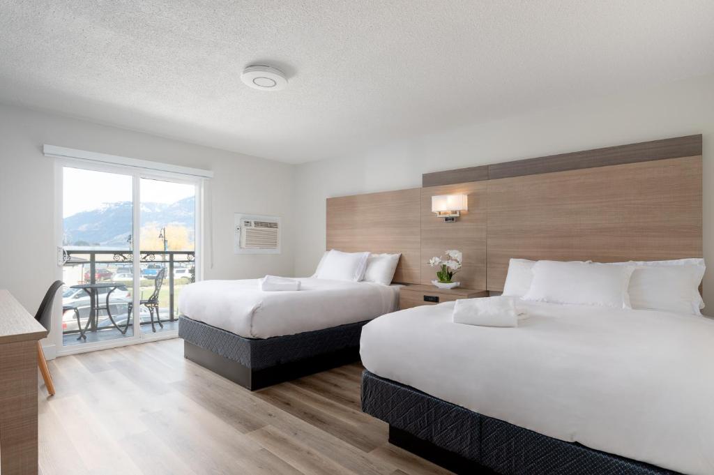 two beds in a hotel room with a balcony at Harrison Grand Motel in Harrison Hot Springs