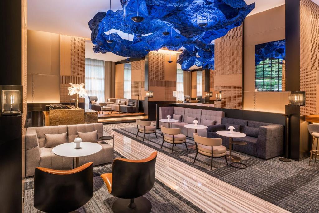 A contemporary hotel lounge with deep sofas, small tables, and a dramatic blue ceiling installation.