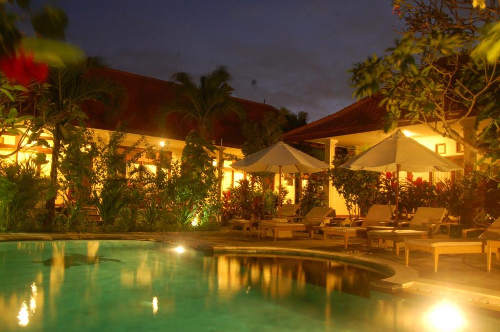 a resort with a swimming pool with chairs and umbrellas at Gunakaya Homestay in Sanur