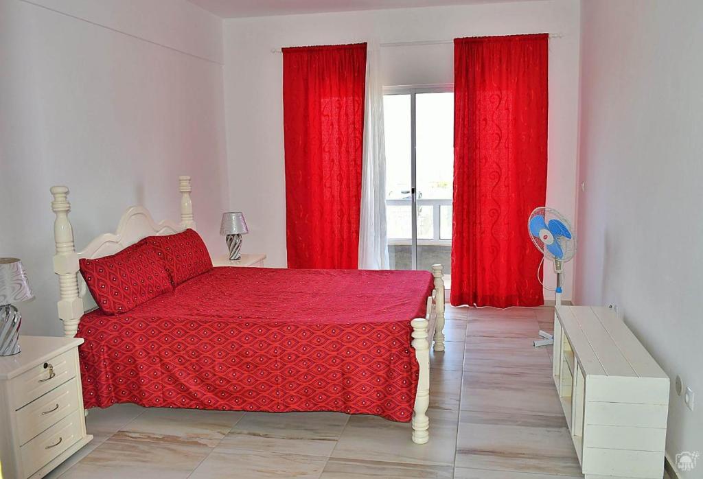 Schlafzimmer mit roten Vorhängen, einem Bett und einem Fenster in der Unterkunft TARRAFAL SN TOUR in Tarrafal