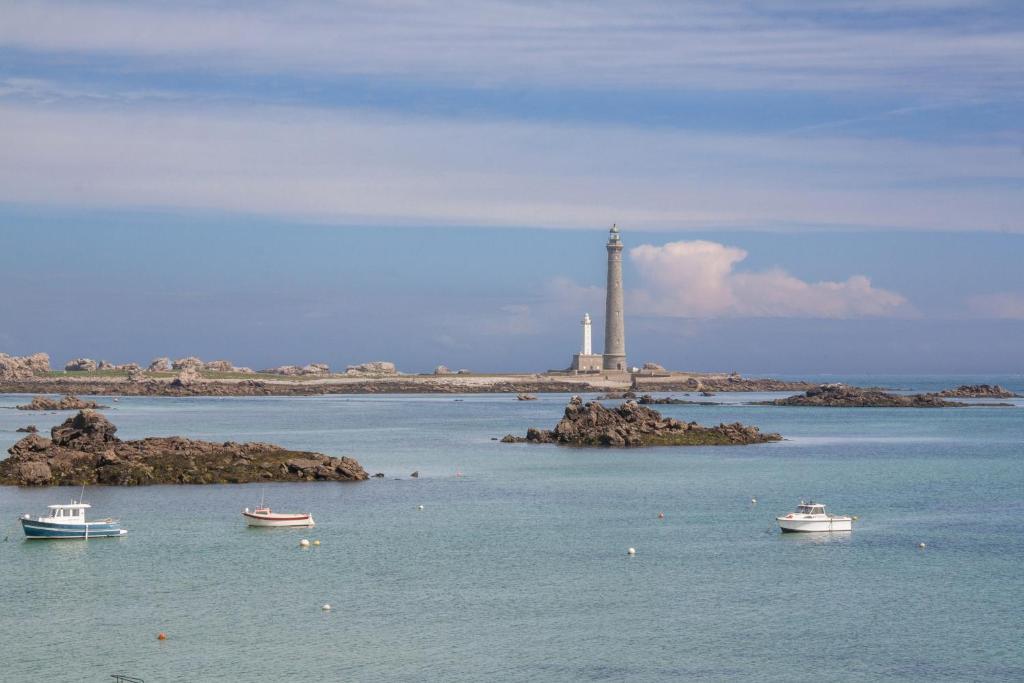 a lighthouse in the ocean with boats in the water at TY COAT - Maison neuve avec vue mer, piscine et bain nordique in Saint-Pabu