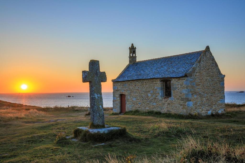an old stone church with a cross in front of a sunset at TY COAT - Maison neuve avec vue mer, piscine et bain nordique in Saint-Pabu