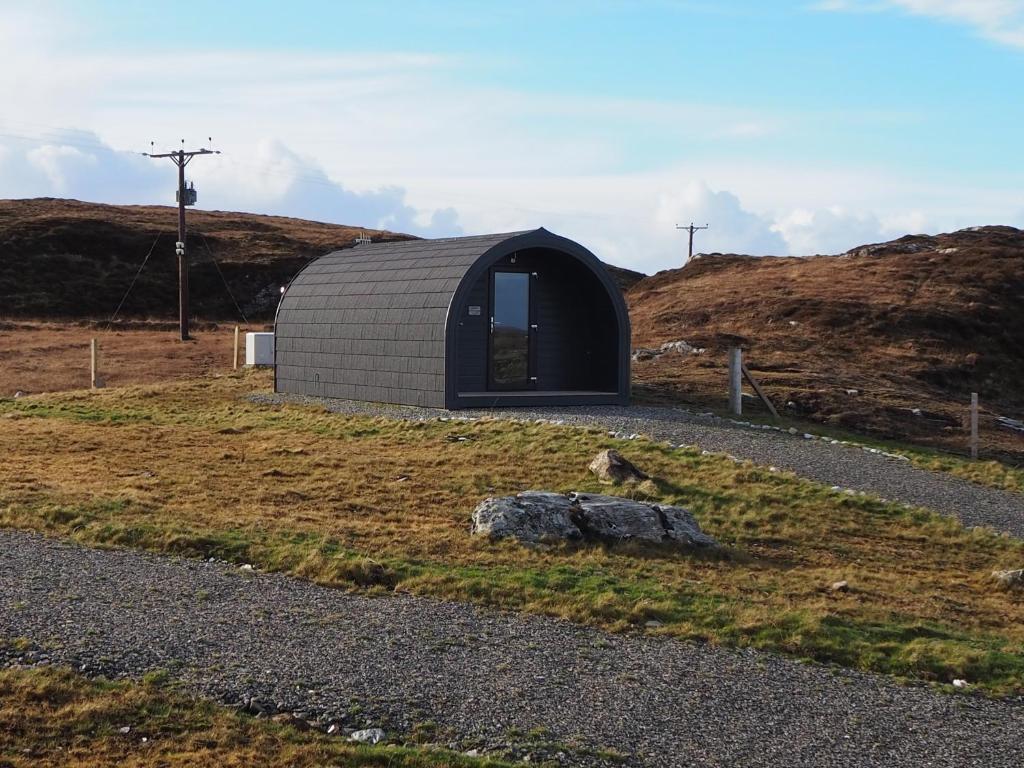 a cat sitting on a rock in front of a building at Grimsay Glamping, North Uist - Pod Ruadh in Rossinish