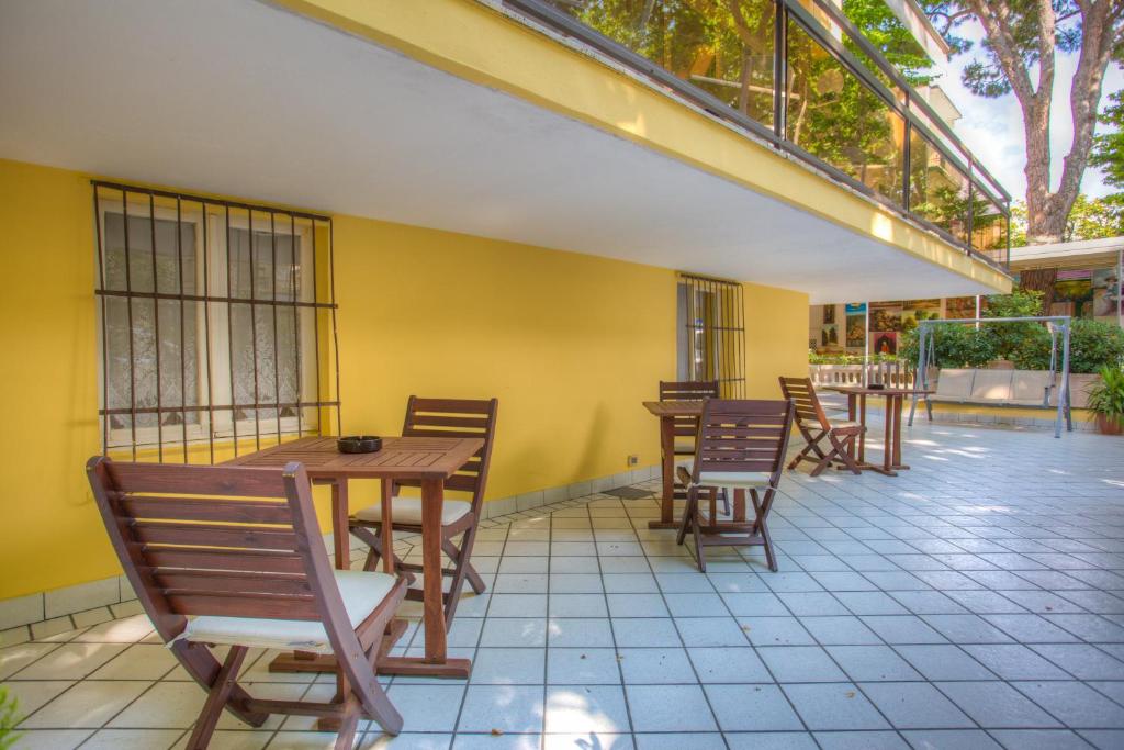 a patio with wooden tables and chairs and a yellow wall at Hotel Tiziana in Rimini