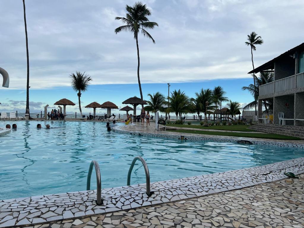a swimming pool next to a beach with palm trees at Village Gales Prive Maragogi in Maragogi