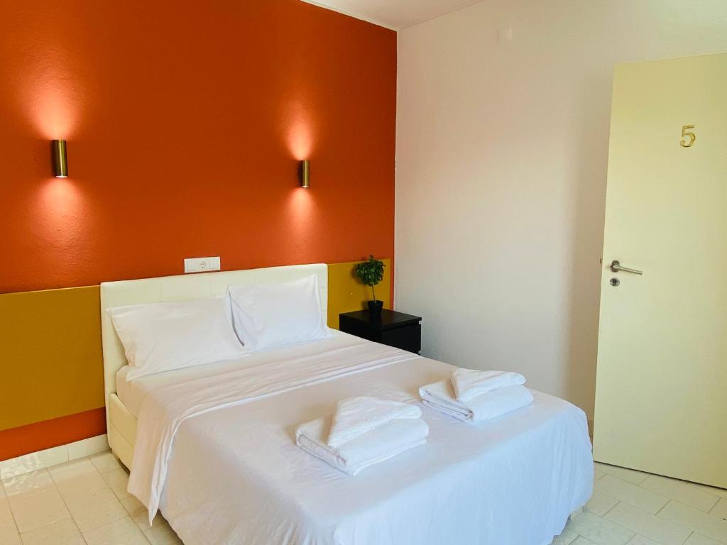 1 dormitorio con cama blanca y pared de color naranja en Central Atlantic Beach Guesthouse, en Costa da Caparica