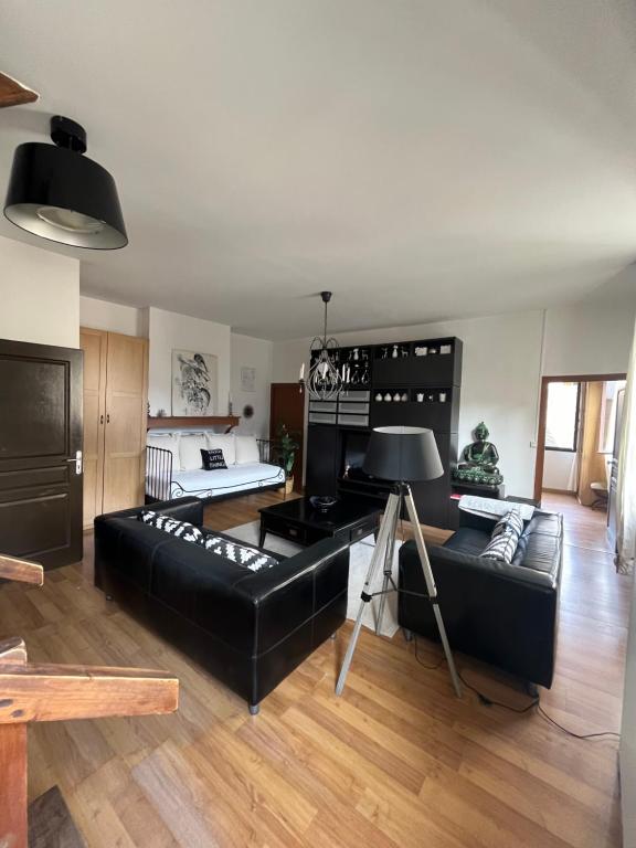 ein Wohnzimmer mit einem schwarzen Ledersofa und Holzböden in der Unterkunft Maison Jehan-Séré in Tarascon-sur-Ariège