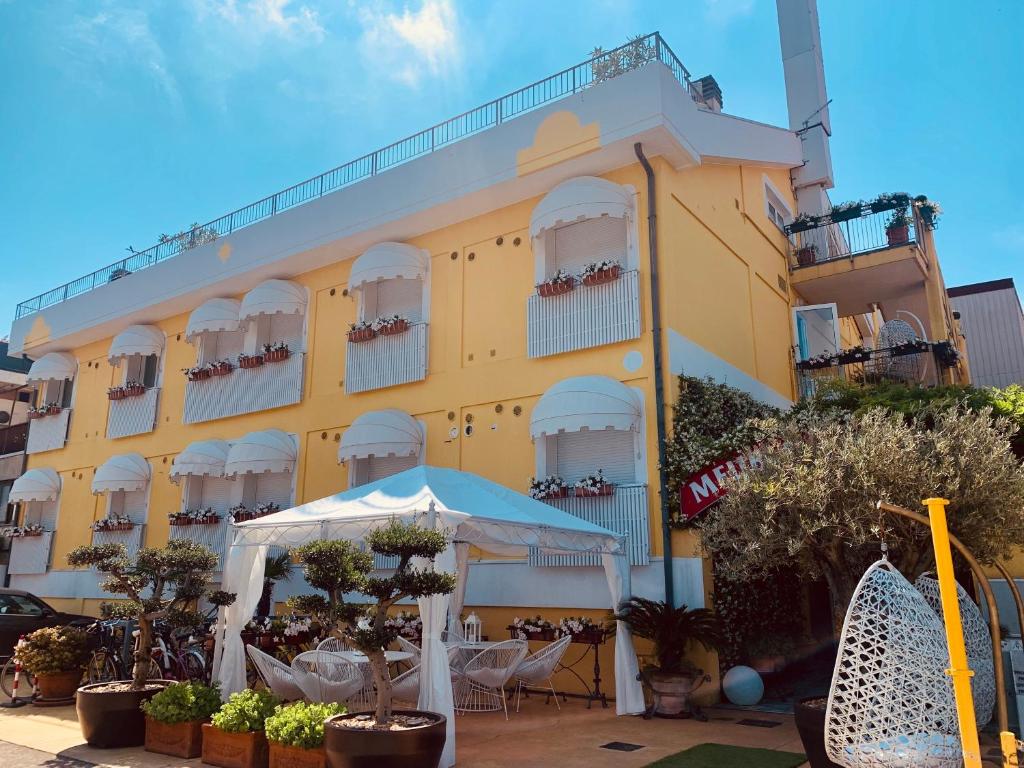 żółty budynek ze stołami i krzesłami przed nim w obiekcie Meublè Tripoli w Grado