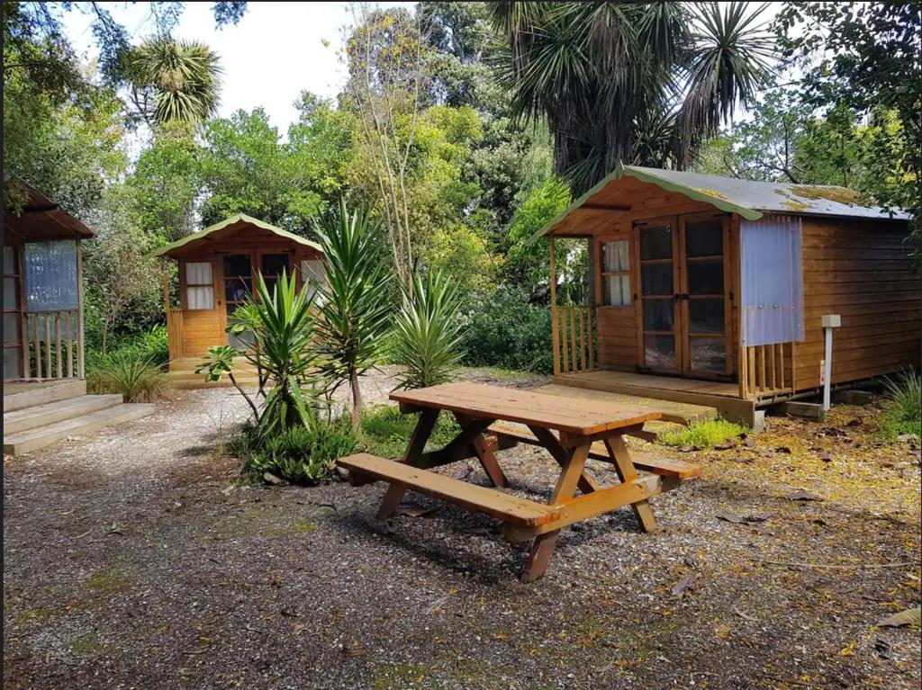 una mesa de picnic de madera frente a una cabaña en Cozy Glamping Cabins en Motueka