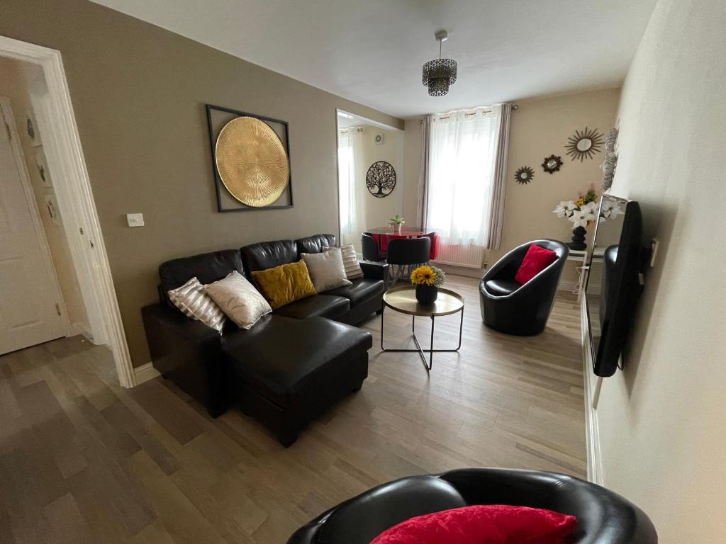 een woonkamer met een zwarte leren bank en stoelen bij Glastonbury Town Centre, Lovely 2 Bedroom Apartment in Glastonbury