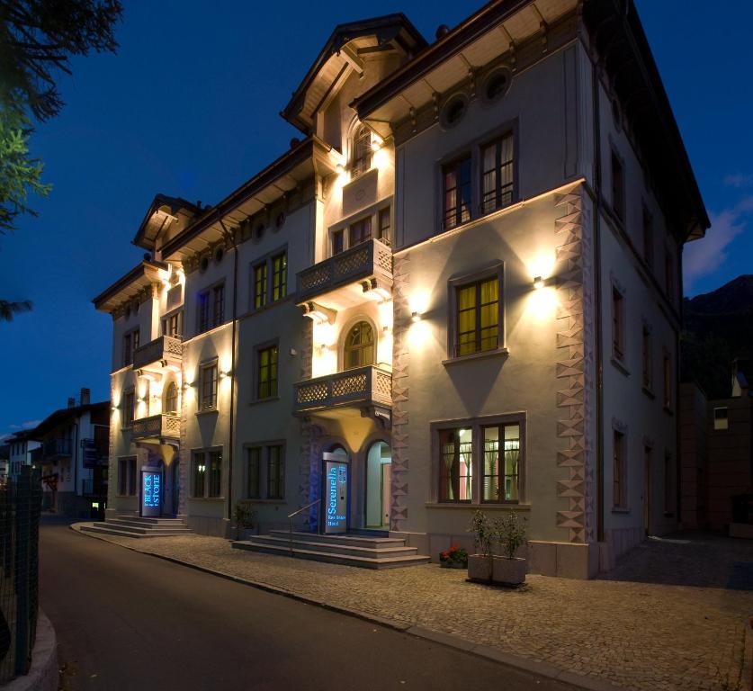 Un grand bâtiment blanc avec des lumières allumées la nuit dans l'établissement Residence Hotel Serenella, à Aprica