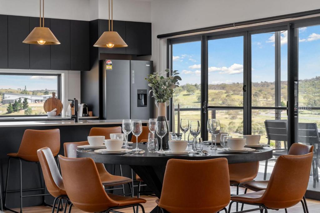 Un comedor con mesa y sillas y ventanas. en 1B Alpine View Retreat - 4BR Luxurious Escape l Mountain Views l Fast WiFi, en Jindabyne