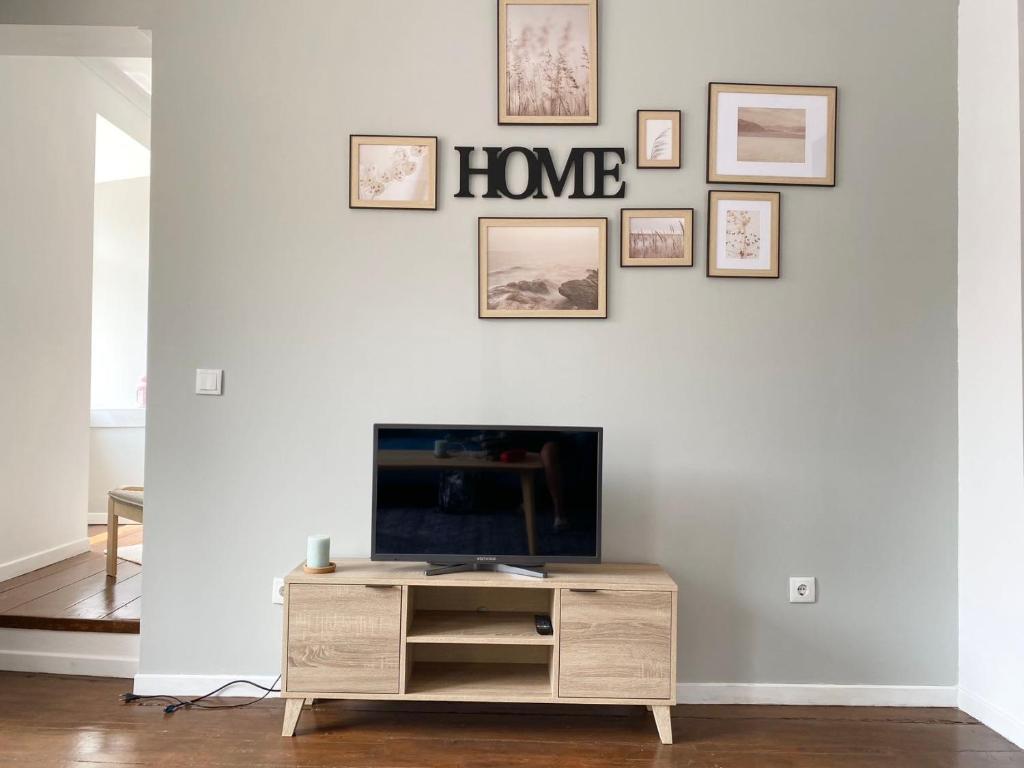 a living room with a tv on a white wall with framed pictures at Ady house in Setúbal