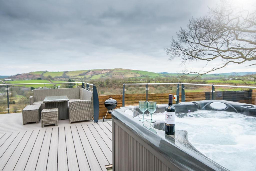 a hot tub on a deck with wine glasses at Tranquil house with hot tub BBQ wheelchair access in Llandeilo