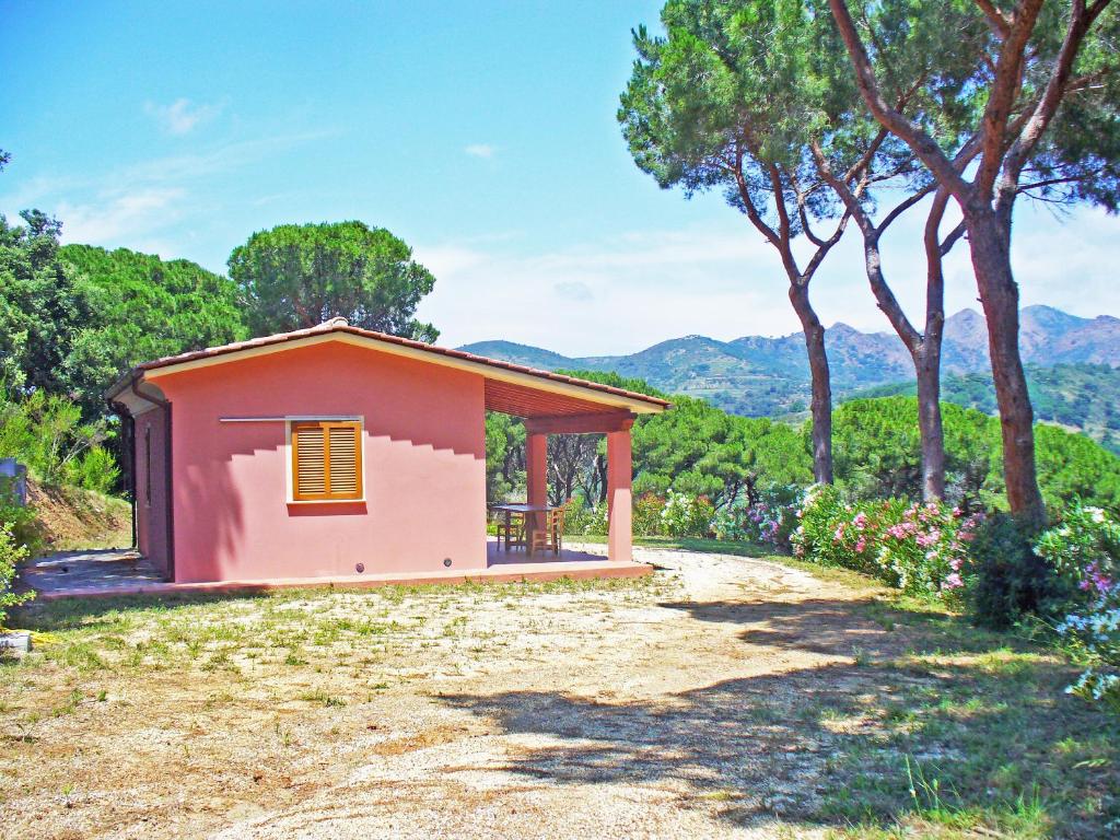 una pequeña casa rosa con árboles y montañas en el fondo en Villetta Giada, en Capoliveri