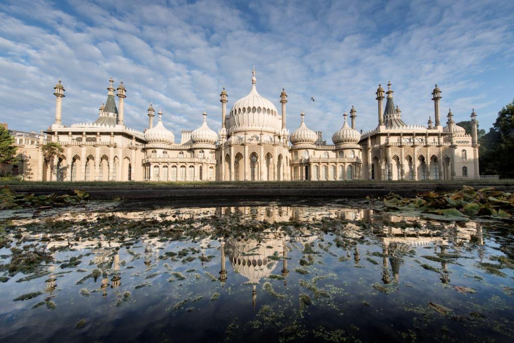 a large white building with a reflection in a pond at Maldron Hotel Brighton City Centre in Brighton & Hove