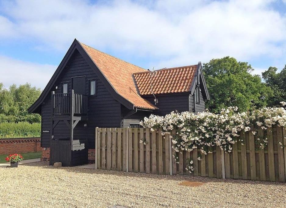 a black house with a wooden fence and flowers at South Barn, Nr Southwold in Southwold