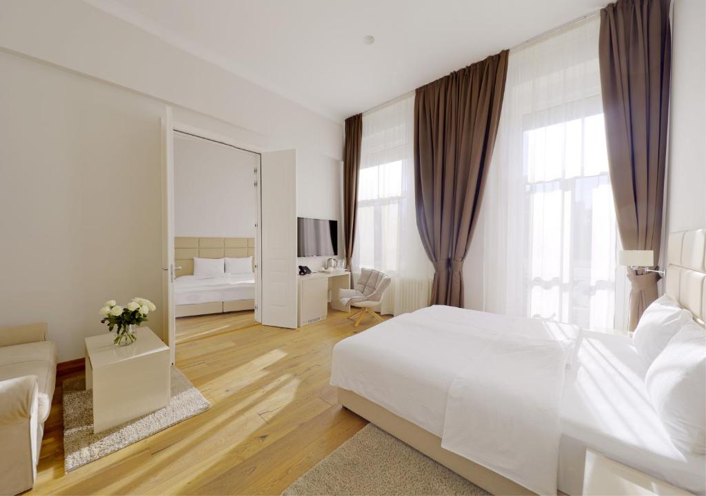 a white bedroom with a large white bed and a mirror at Lanterna Rooms City Center in Novi Sad