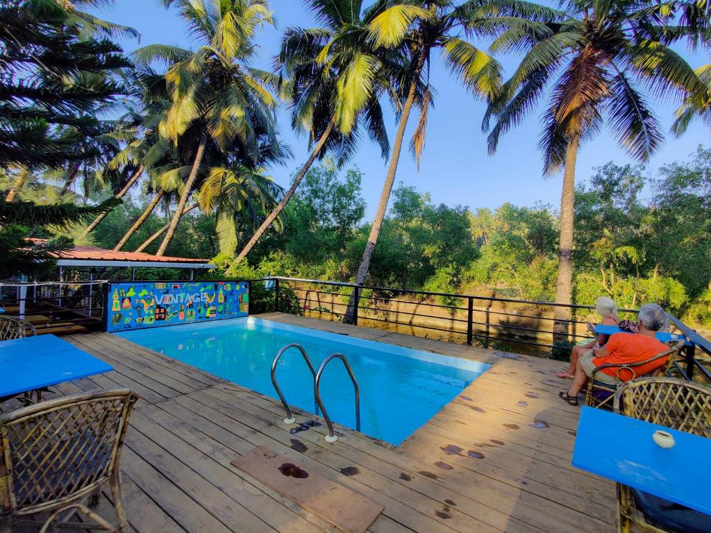 a couple sitting on a deck next to a swimming pool at Vintage Beach Resort in Agonda