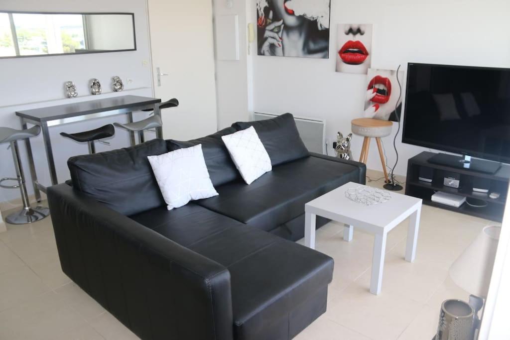 un salon avec un canapé noir et une télévision dans l'établissement Appartement 408, Natura beach au village naturiste, au Cap d'Agde