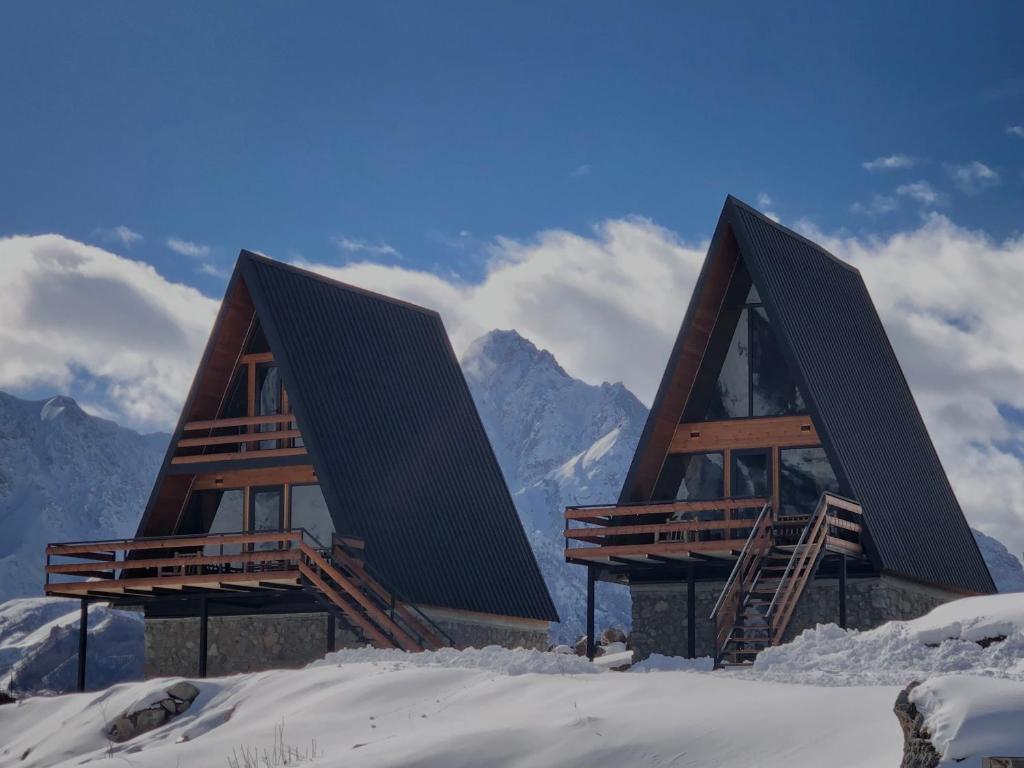 Deux maisons dans la neige avec des montagnes en arrière-plan dans l'établissement Arsha View, à Kazbegi