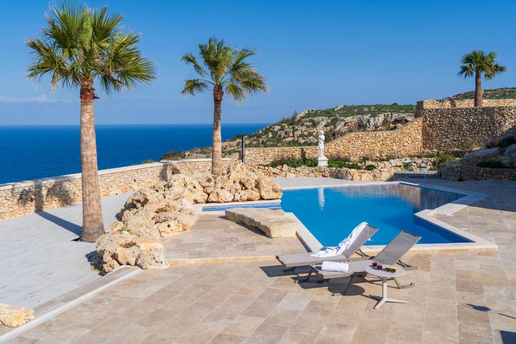 a pool with two lounge chairs and palm trees at L-Eremita Boutique Hotel in Qala