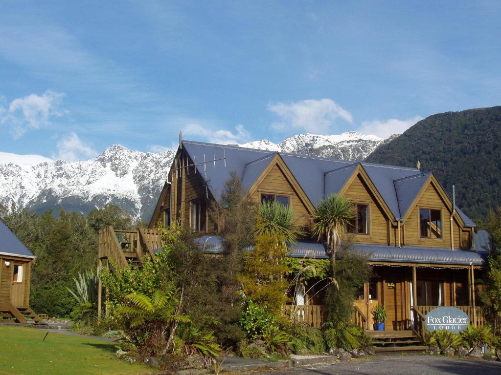 una gran casa de madera con montañas en el fondo en Fox Glacier Lodge, en Fox Glacier