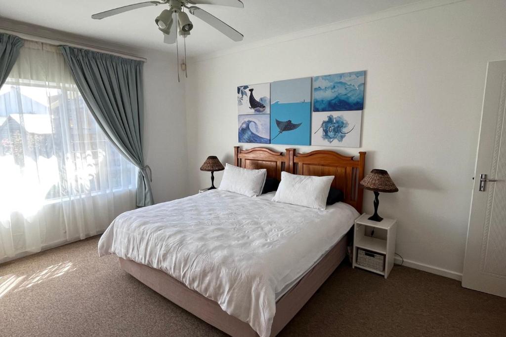 een slaapkamer met een bed met witte lakens en een plafondventilator bij Relax @ Jbay in Jeffreys Bay