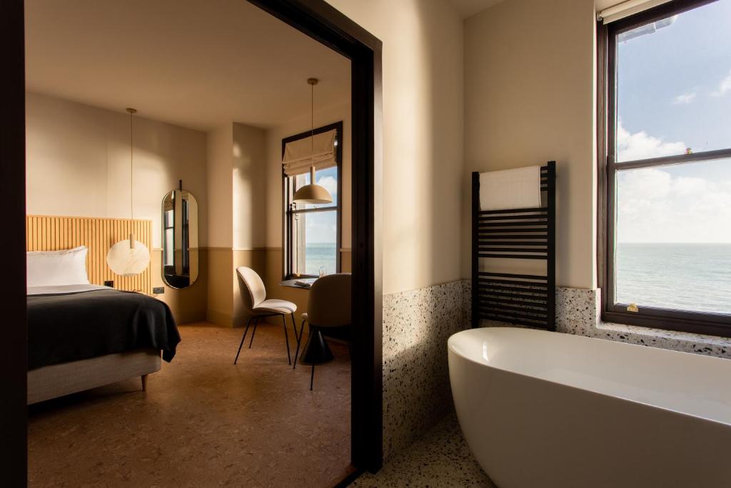 een badkamer met een bad, een bed en een raam bij Port Hotel in Eastbourne