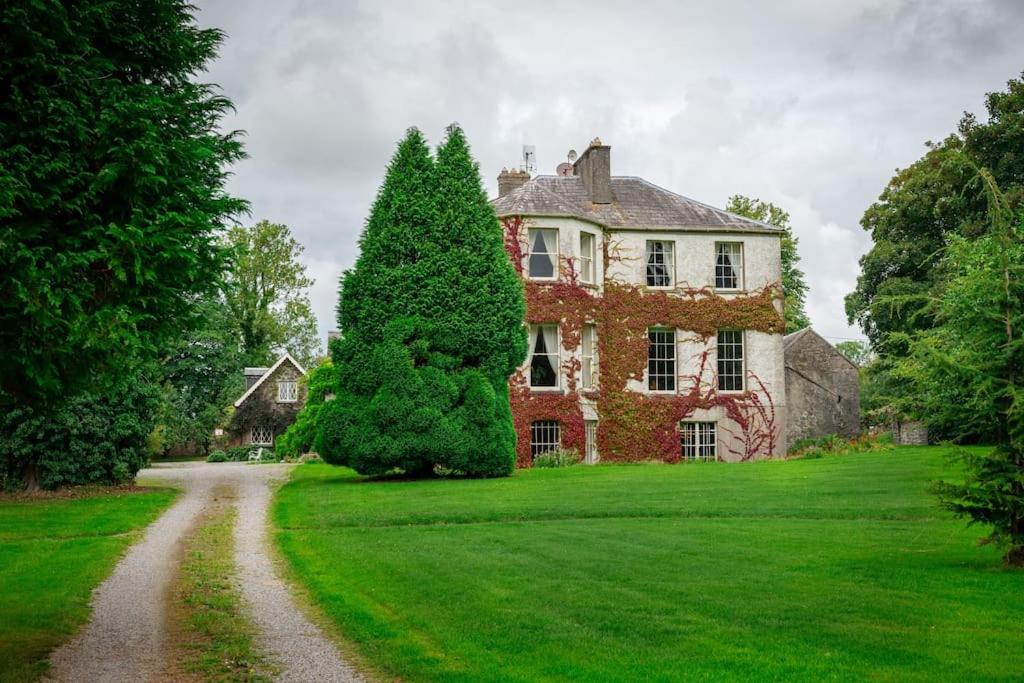 a large house on a green lawn with a dirt road at Kilfane Glebe House in Thomastown