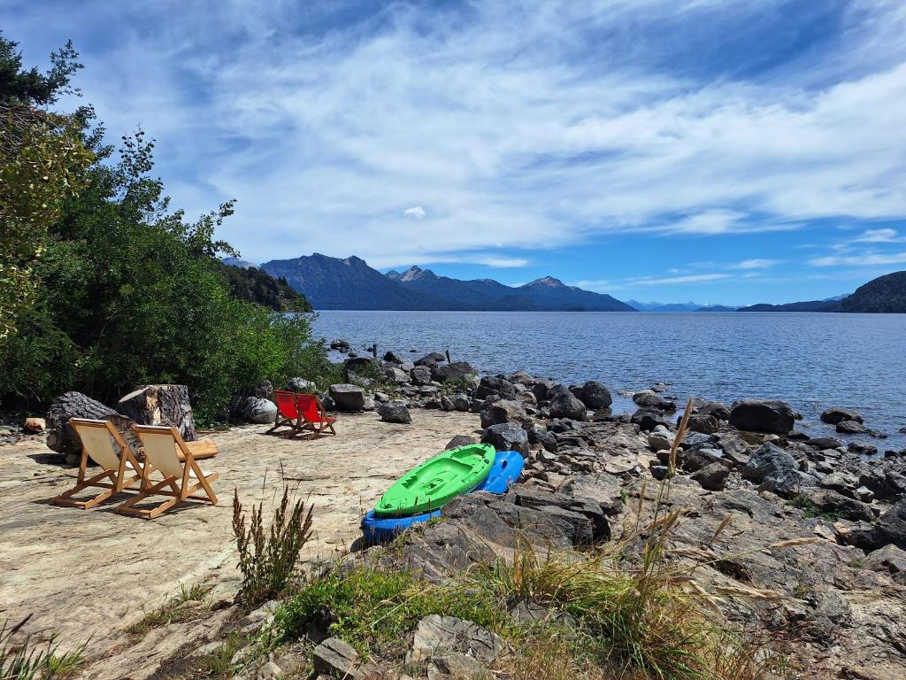 ein Strand mit Stühlen und ein grünes Boot am Ufer in der Unterkunft Eco Cabañas Fardos del Bosque in San Carlos de Bariloche