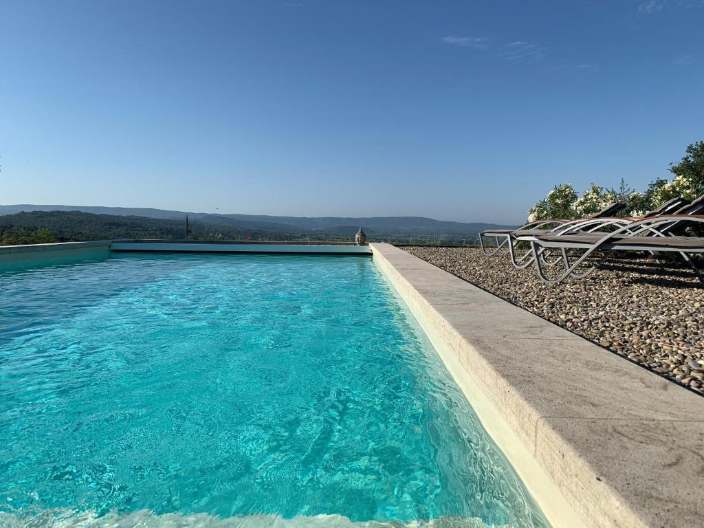 - une piscine d'eau bleue à côté d'une table dans l'établissement La Bergerie des Pottiers. Mas rénové climatisation Piscine, à Crillon-le-Brave