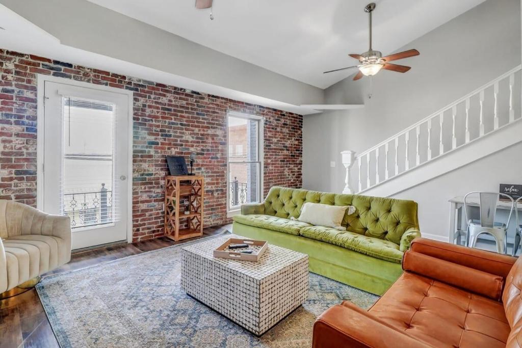 a living room with a green couch and a brick wall at Eagle's Landing Loft-Downtown Above Bull & Barrel in Statesboro