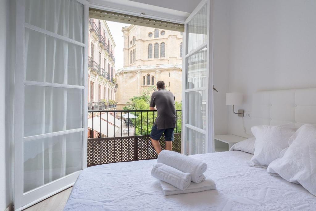 a man standing on a balcony looking out of a bedroom window at Cathedral Suites in Málaga
