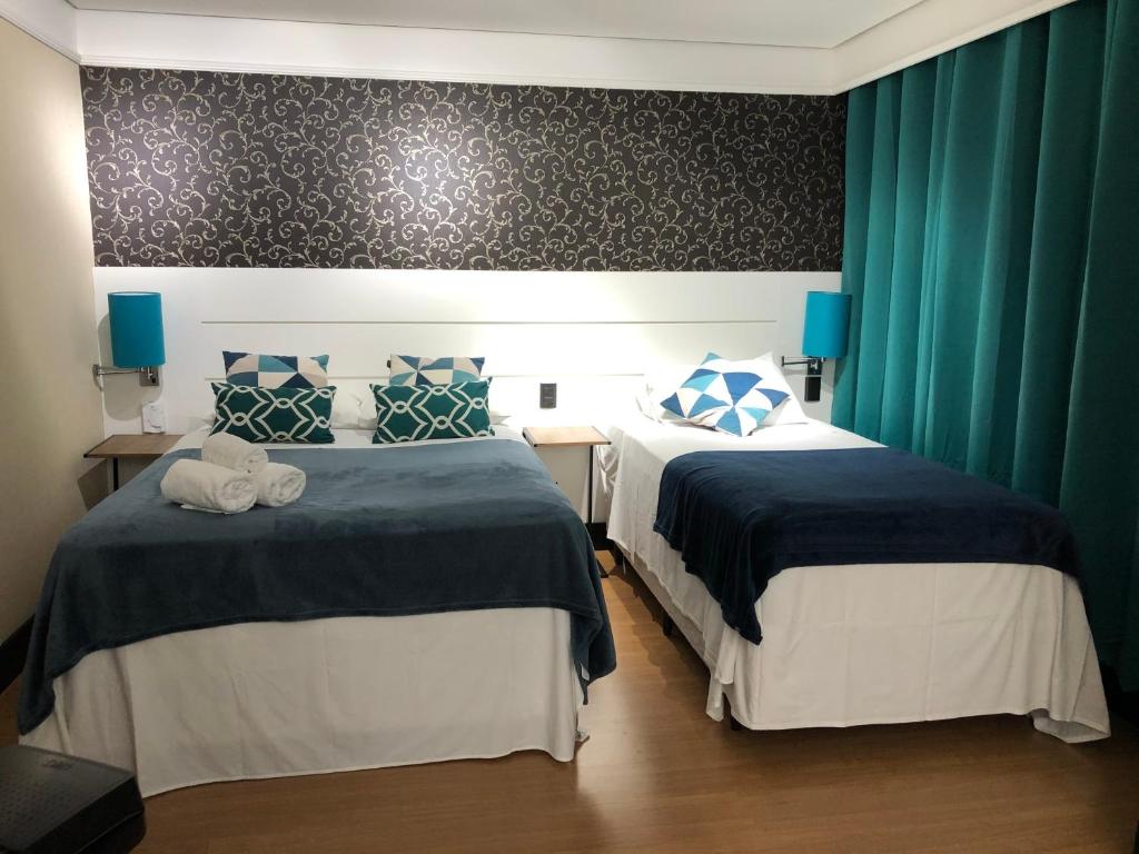 Duas camas num quarto com cortinas verdes e candeeiros azuis em Quarto de hotel entre os Shoppings Vila Olimpia e JK Iguatemi em São Paulo