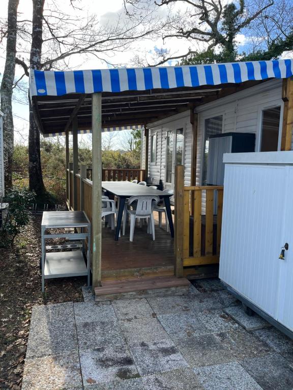 a small house with a table and a blue awning at Mobilhome camping les petits écureuils 4 étoiles Biscarrosse in Biscarrosse