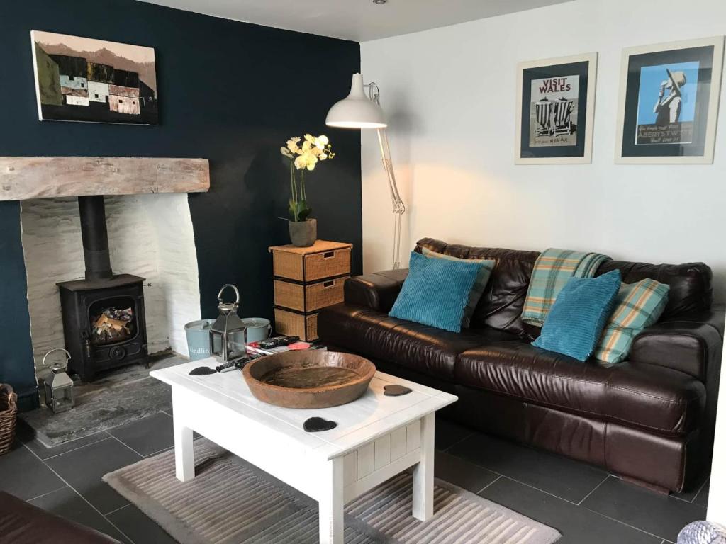 a living room with a leather couch and a fireplace at Cilrhiw, Seaside Stone Cottage in Llangrannog in Llangrannog