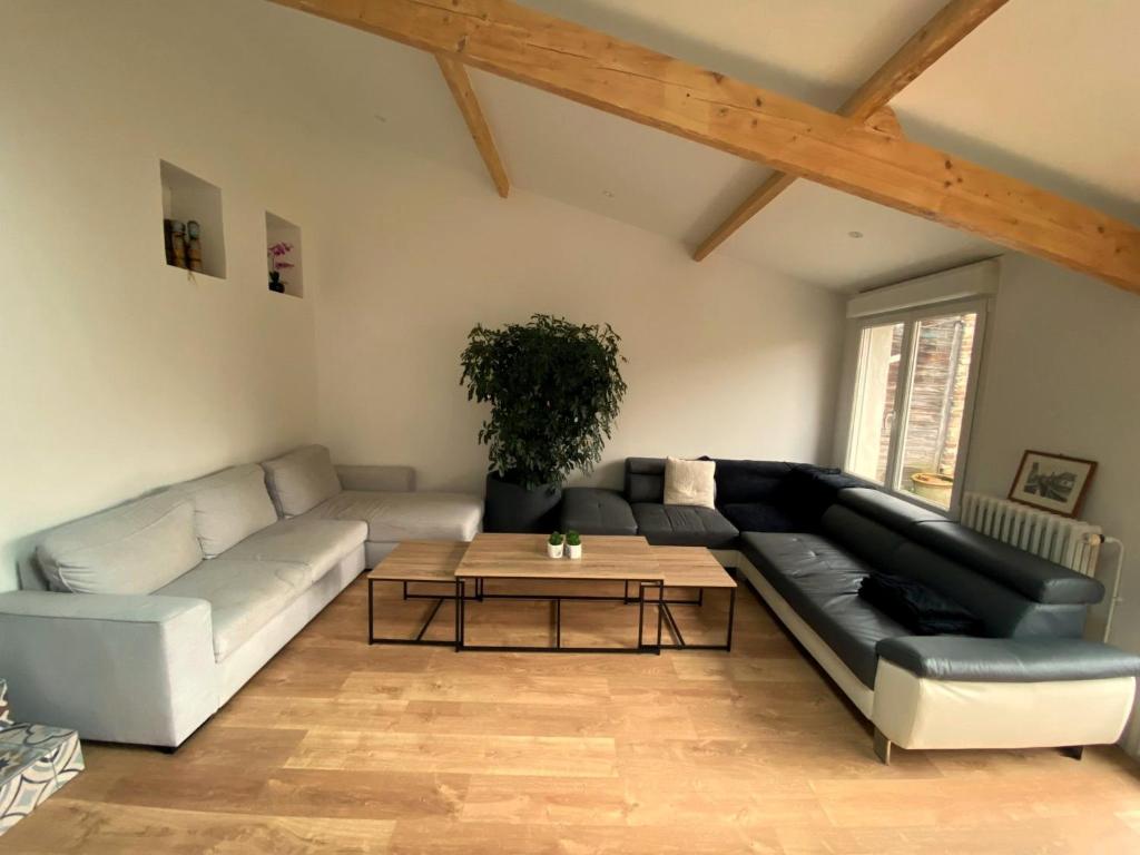 a living room with a black leather couch and a table at Maison 4 chambres au calme beau jardin et studio in Cagny