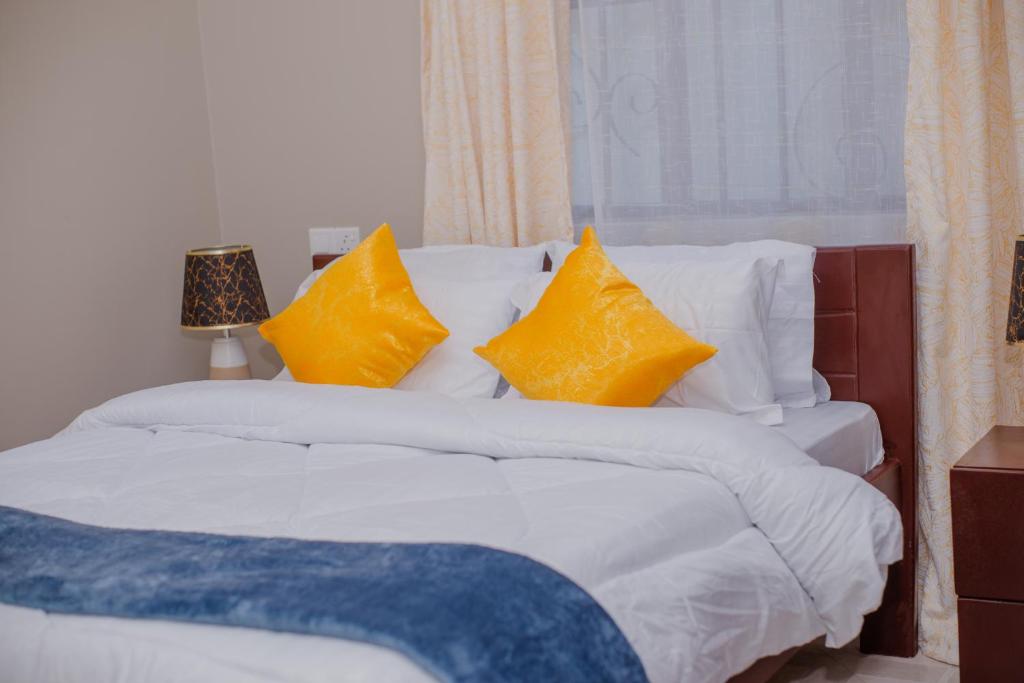 uma cama com lençóis brancos e almofadas amarelas em Sisi's Homes em Arusha